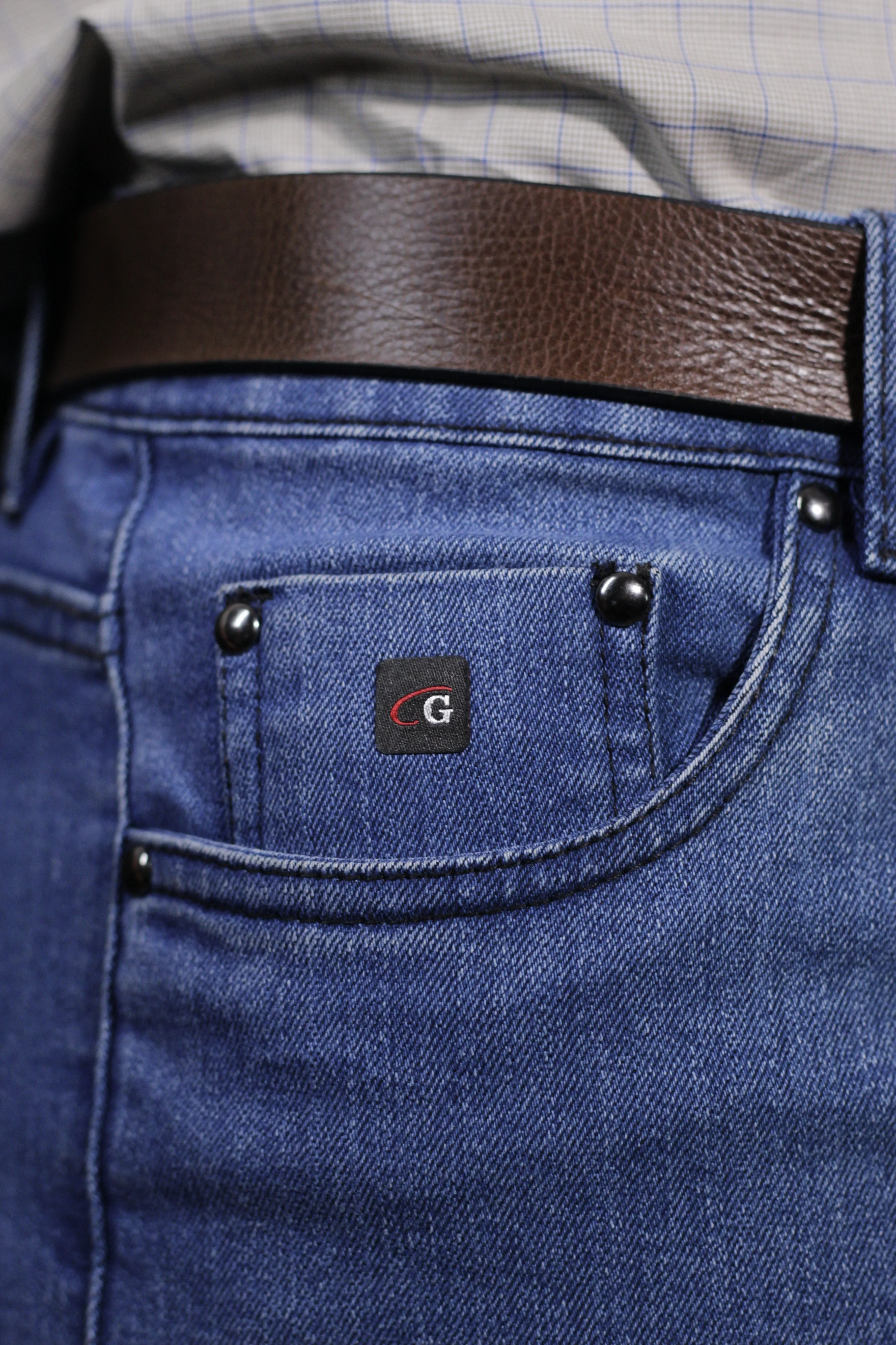 Detalhe de calça social azul com bolso, textura e cinto.